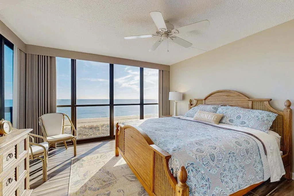 A bedroom with a wooden bed and large windows overlooking the ocean.