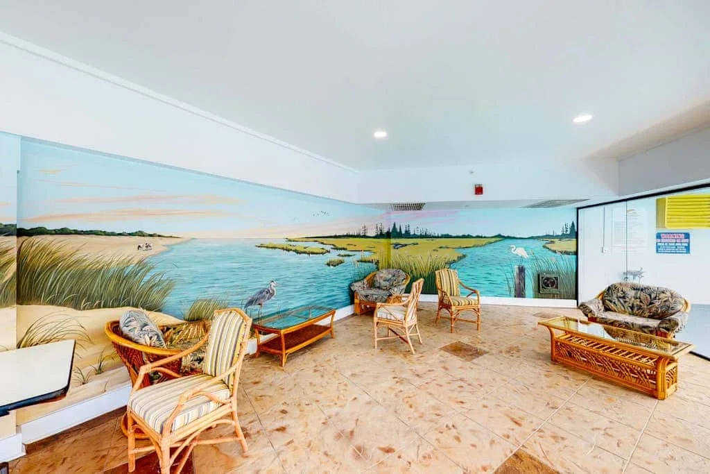 A bright indoor seating area features a large mural of a coastal landscape.