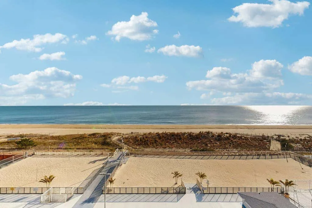 A sandy beach and ocean stretch beneath a partly cloudy sky.