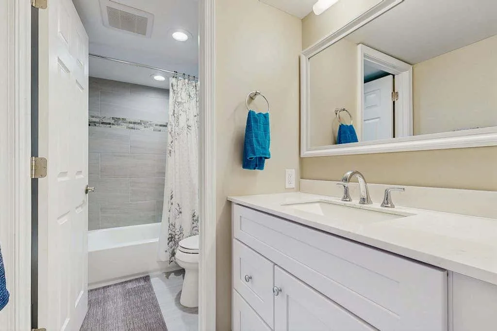 A bathroom vanity with a sink and mirror beside a tiled bathtub and shower.
