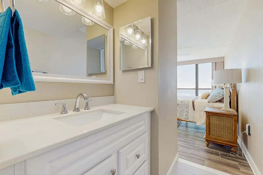 A bathroom vanity with a wide sink counter opens onto a bedroom.