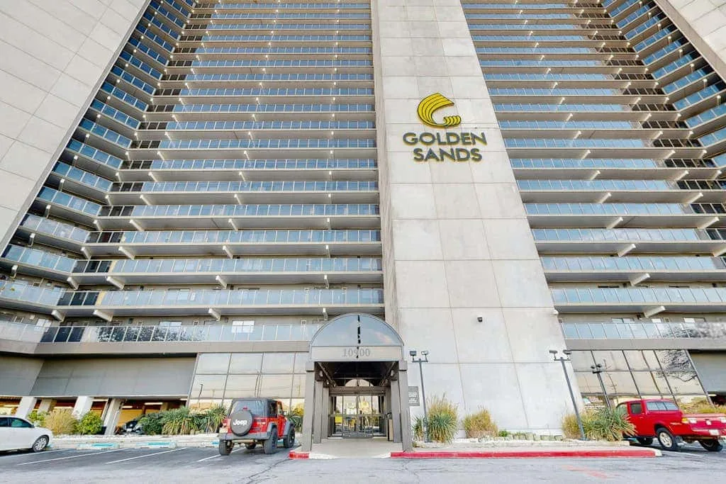 A tall modern building with rows of balconies and a central entrance.