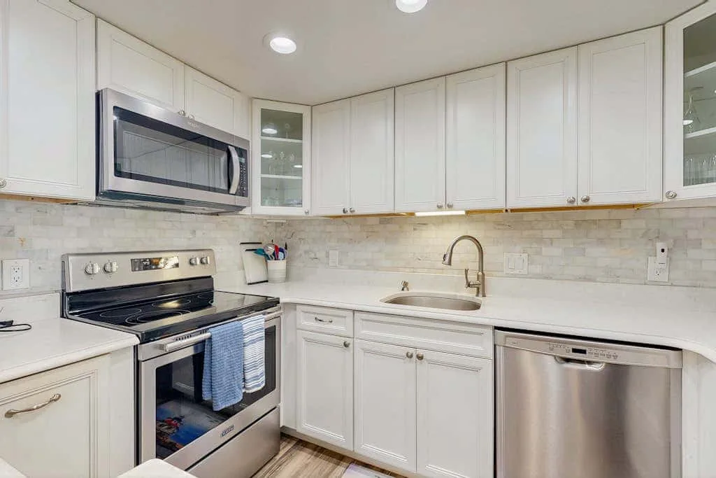 A bright kitchen with white cabinetry, a stove, and a sink.