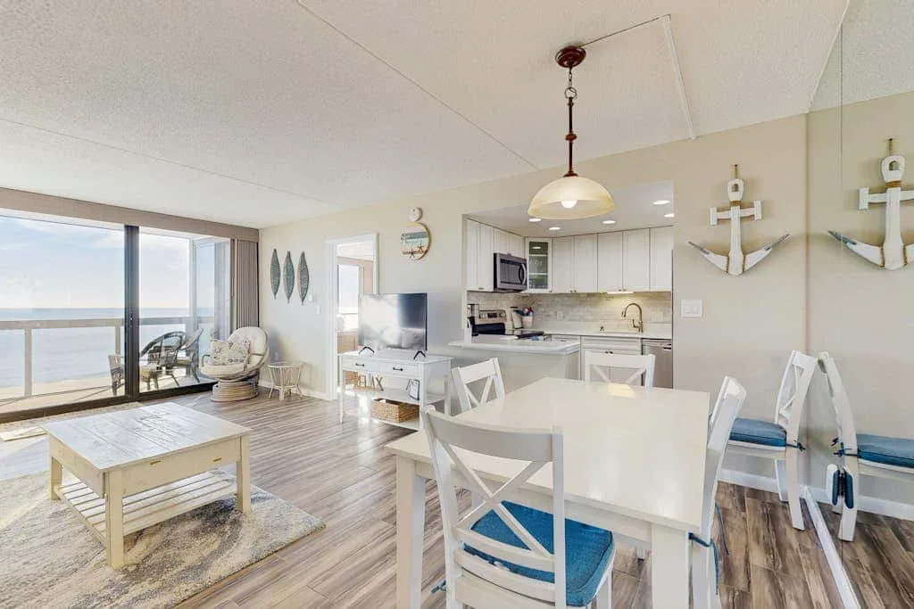 An open-plan dining and living area with a kitchen and large windows overlooking the water.