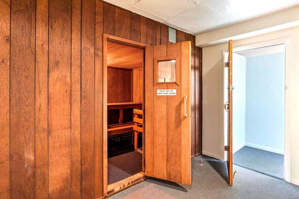 A wood-paneled sauna room with an open door and a glimpse of the interior benches.