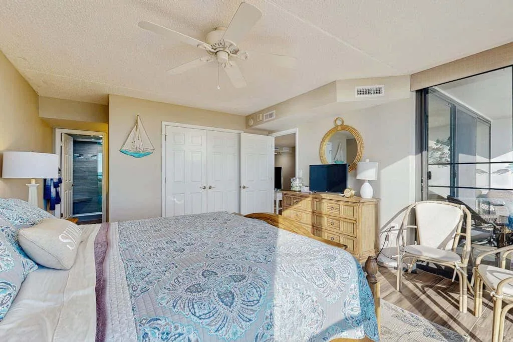 A bedroom with a patterned bedspread, dresser, and glass doors opening to a balcony.