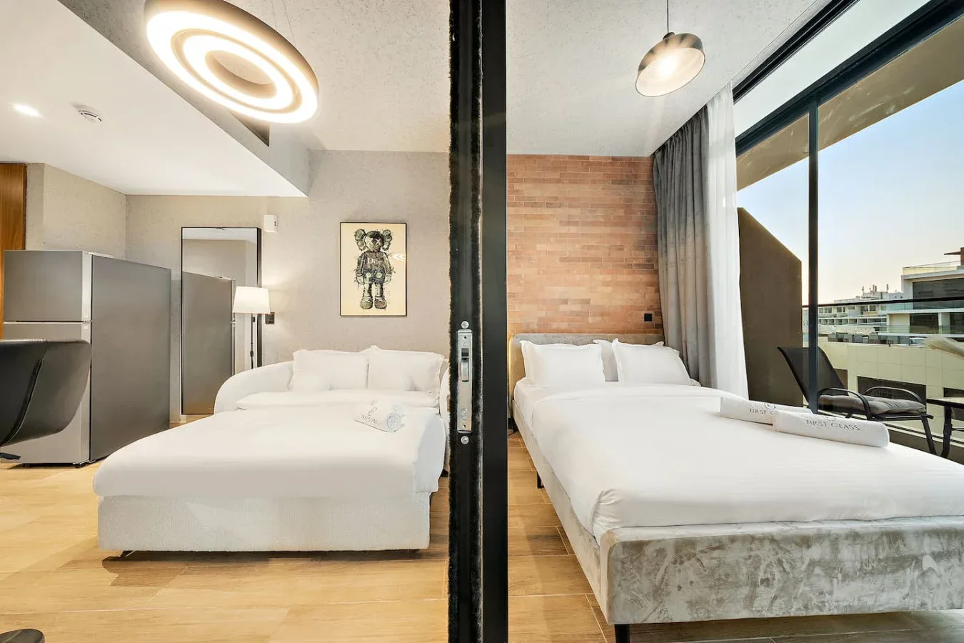 Un dormitorio luminoso con dos camas junto a una ventana de vidrio de piso a techo.