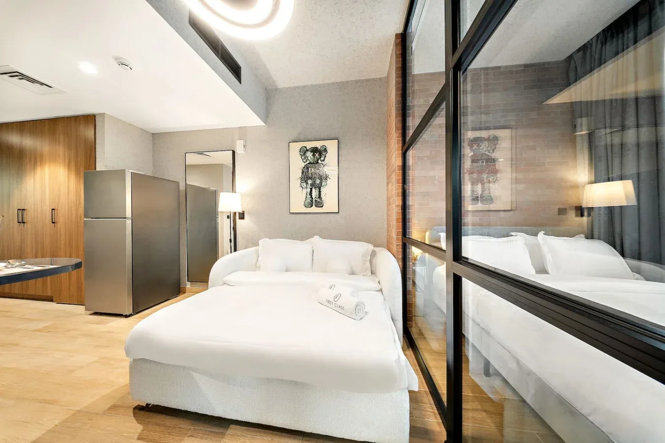Un dormitorio luminoso con una cama blanca junto a una mampara de vidrio.