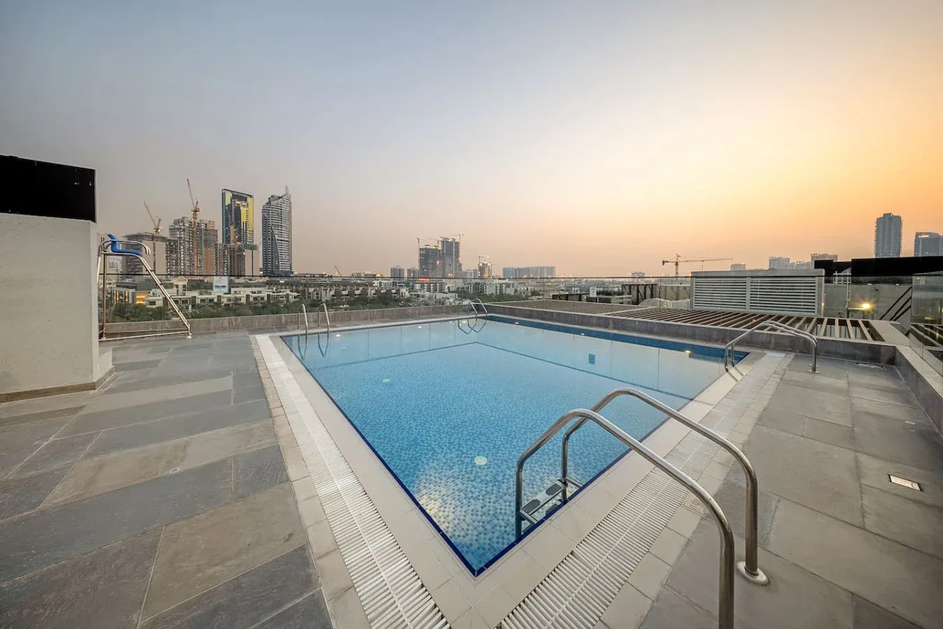 Una piscina en la azotea está junto a una terraza pavimentada, con el horizonte urbano al fondo.