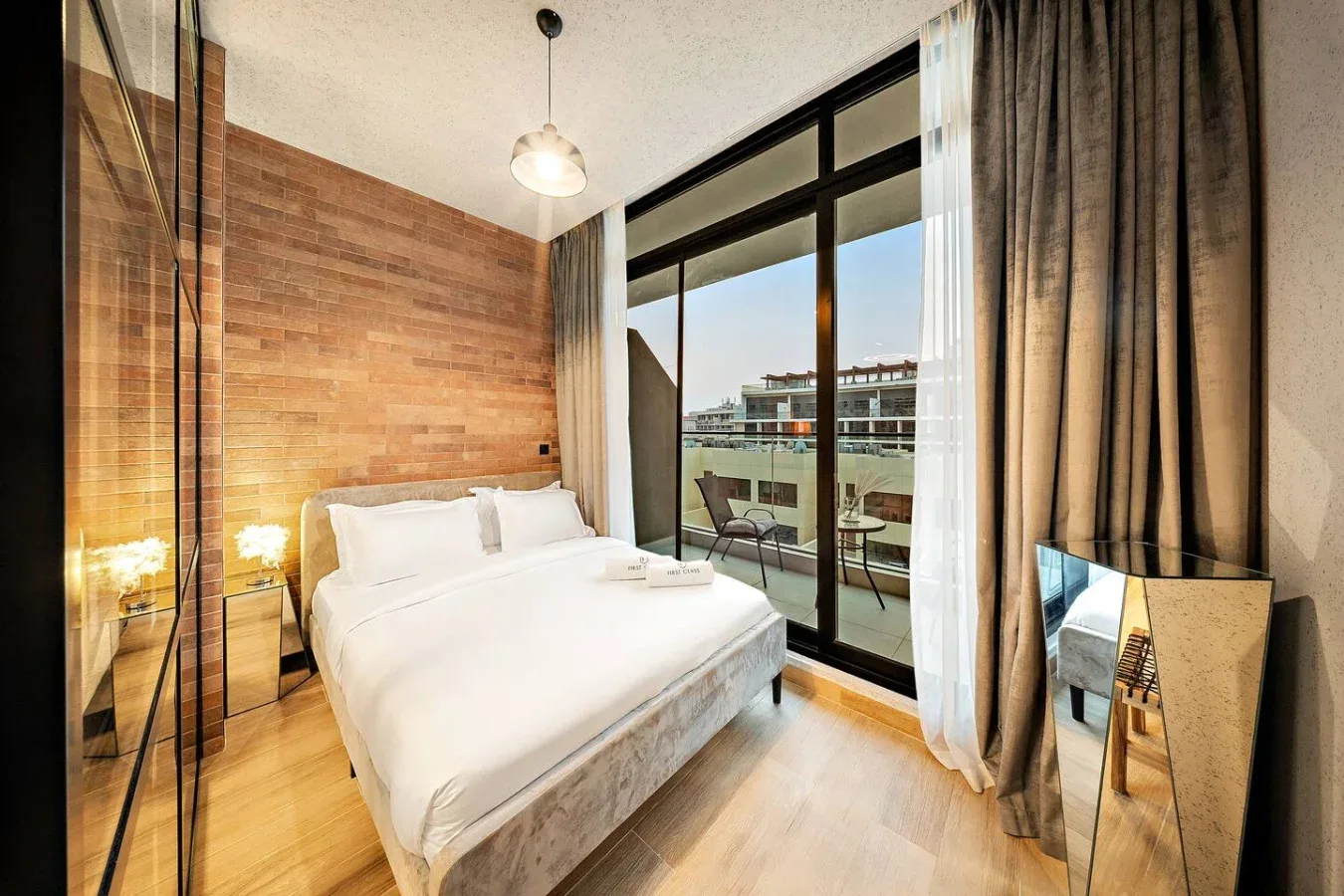 Un dormitorio con una cama bien hecha junto a grandes ventanales y cortinas.