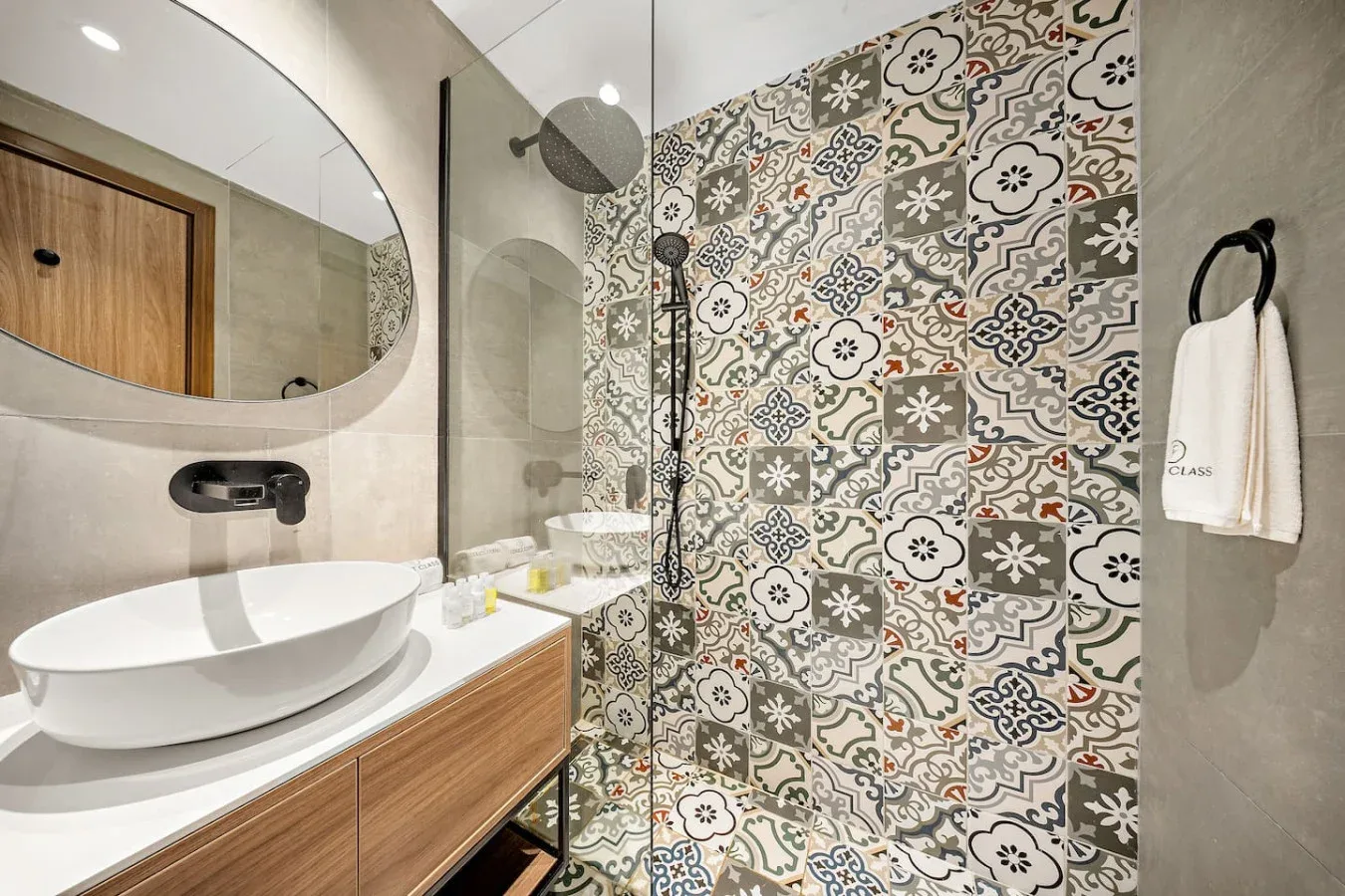 Un baño con lavabo y zona de ducha junto a una pared de azulejos estampados.