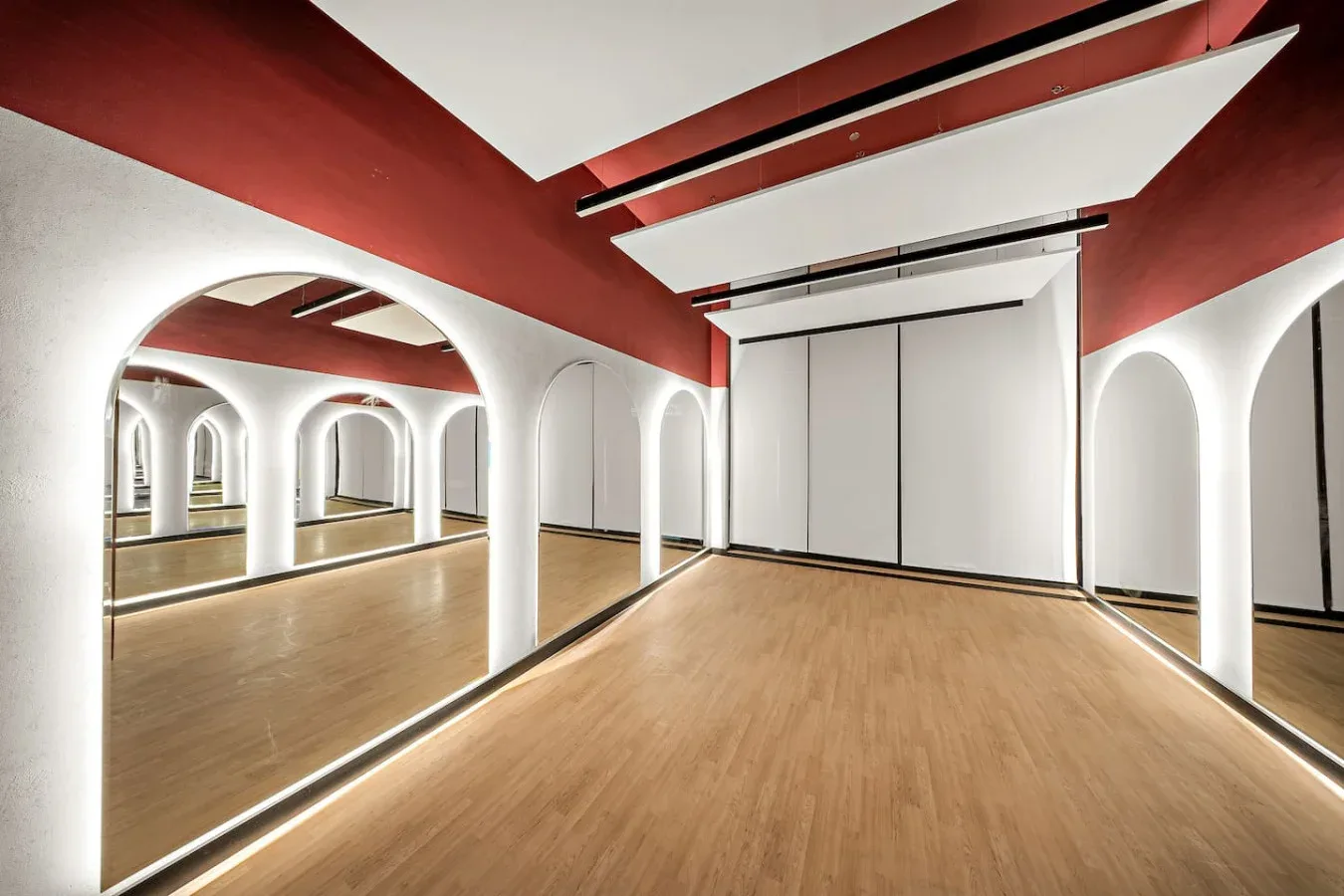 Una sala de estudio con espejos, suelo de madera y aberturas arqueadas blancas.