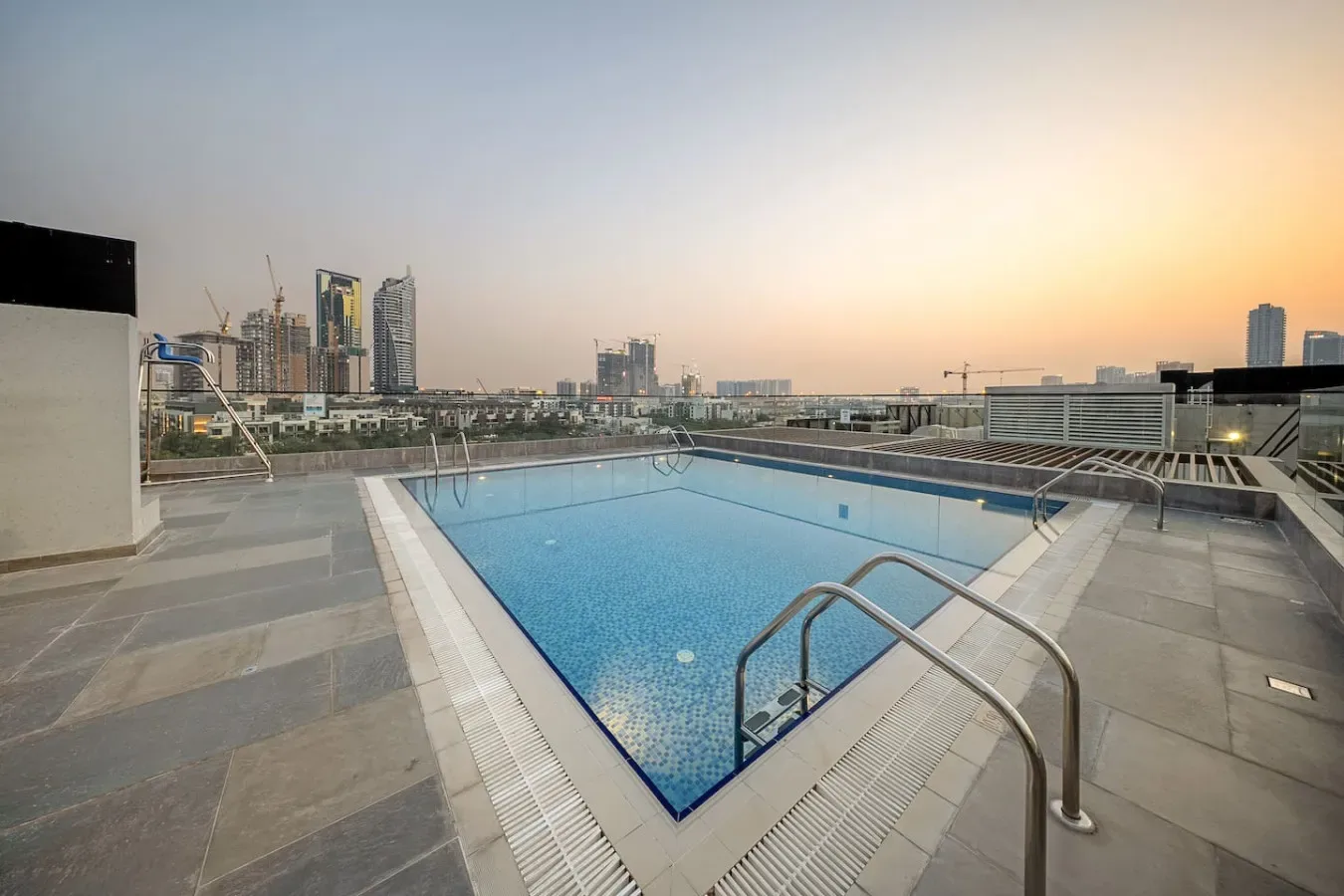 Una piscina en la azotea ofrece vistas de edificios urbanos al atardecer.