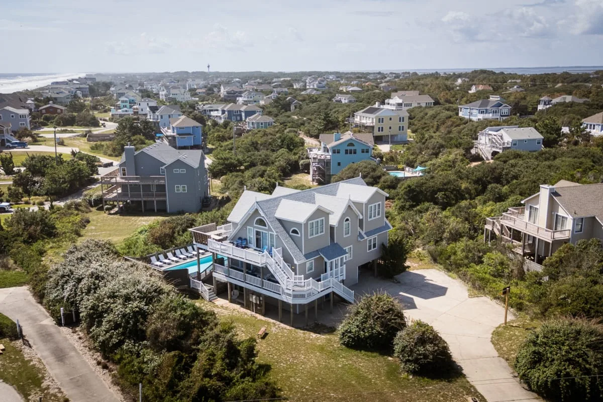 Una vista aérea muestra un vecindario costero con casas, incluida una vivienda gris con piscina.