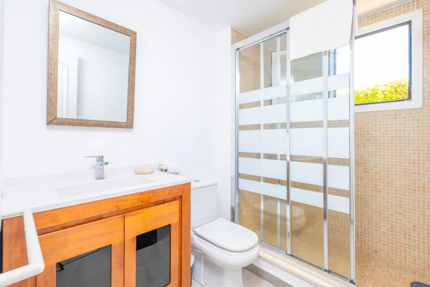 A bright bathroom with a wooden vanity, toilet, and glass shower.