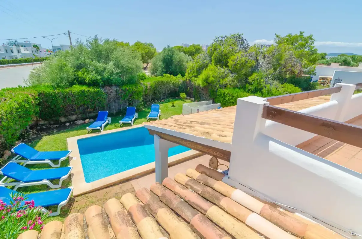 An outdoor pool beside a sun terrace with loungers and surrounding greenery.
