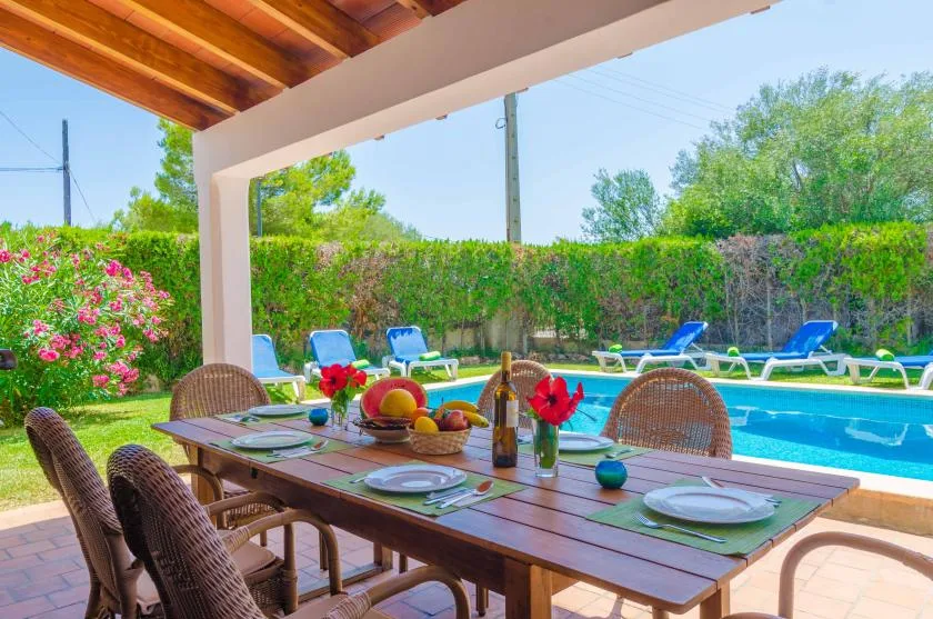 A covered outdoor dining area overlooks a swimming pool and garden.