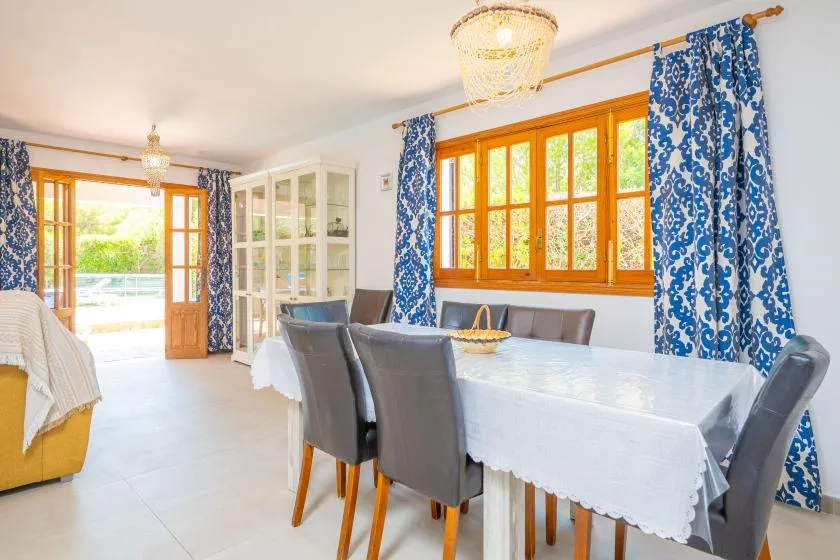 A bright dining area with a long table beside large windows and blue patterned curtains.