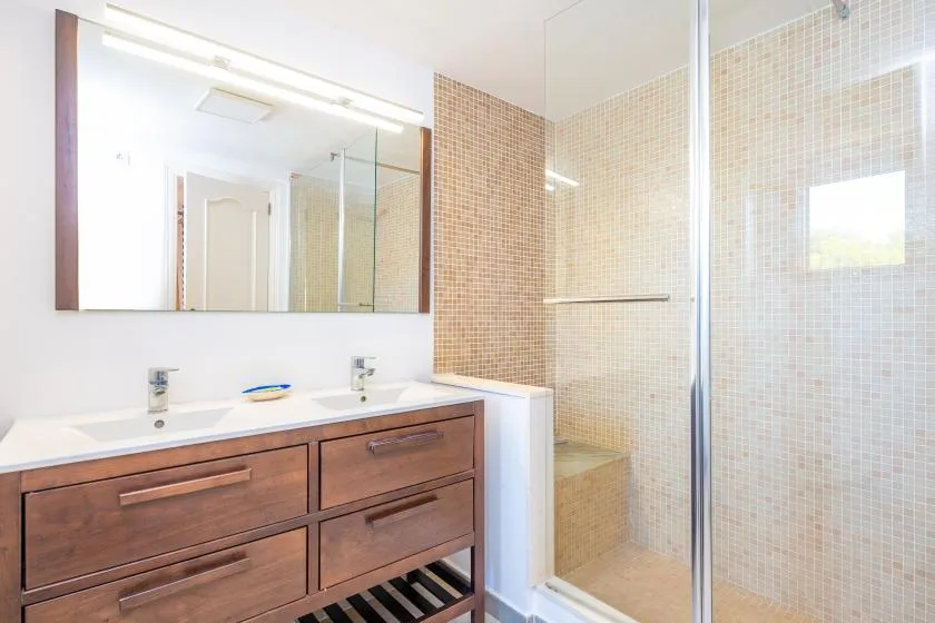 A bathroom with a wood vanity, wide mirror, and tiled shower.