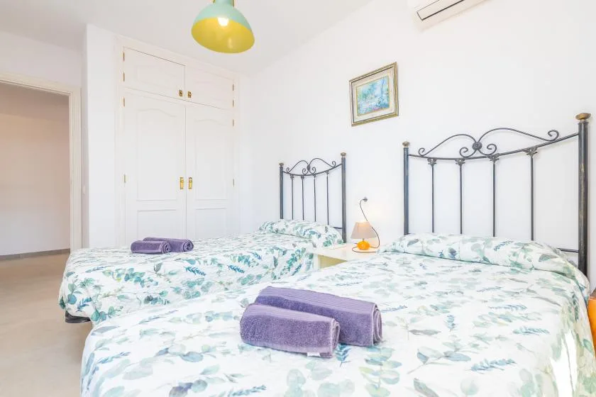 A bright bedroom with two beds covered in light floral bedding.