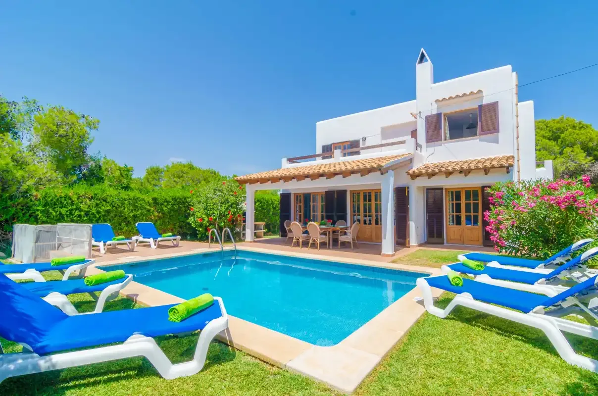 A white two-story house stands beside a swimming pool with lounge chairs.