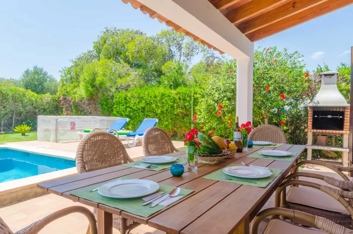 A covered outdoor dining area overlooks a swimming pool and garden.