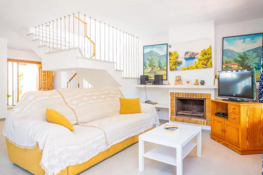 A bright living room with a white-covered sofa, coffee table, and staircase.