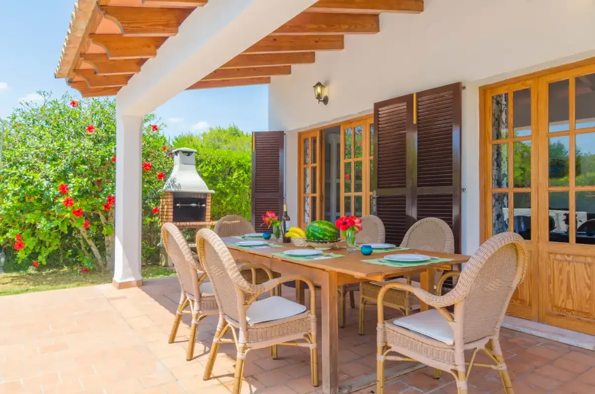 A covered patio with a dining table, woven seating, and a garden view.