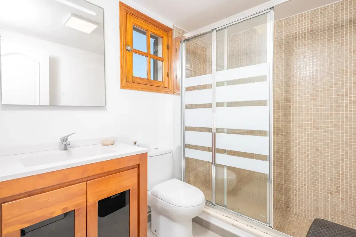 A bright bathroom with a wooden vanity and a glass shower.