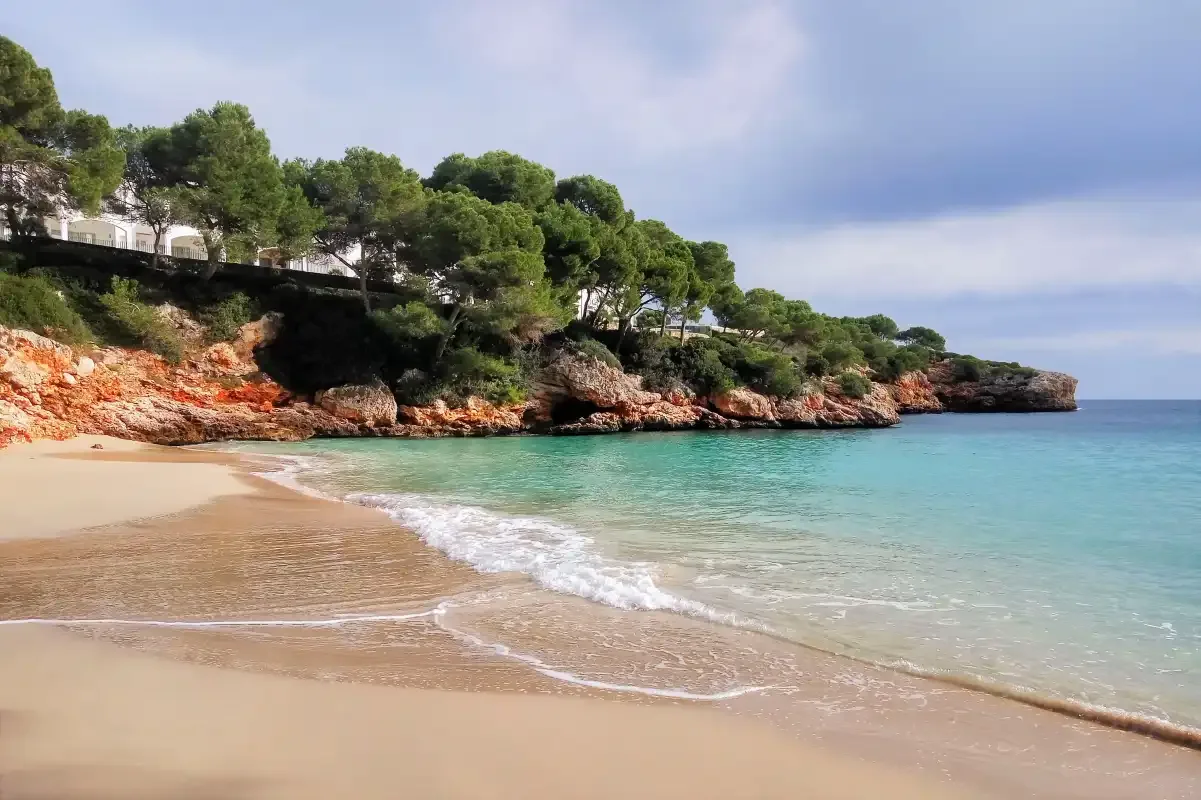A sandy beach curves beside clear turquoise water and a rocky, tree-lined shore.