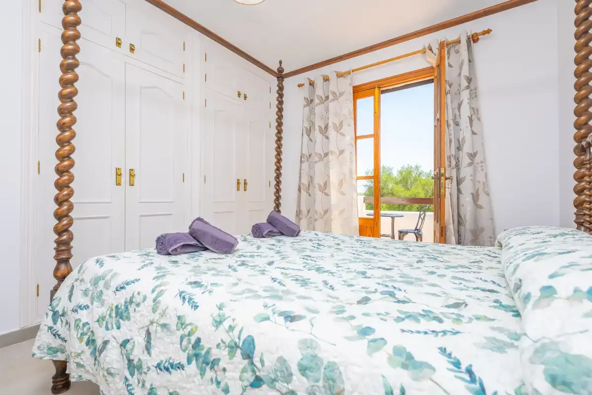 A bedroom with a floral-patterned bedspread and an open window overlooking greenery.