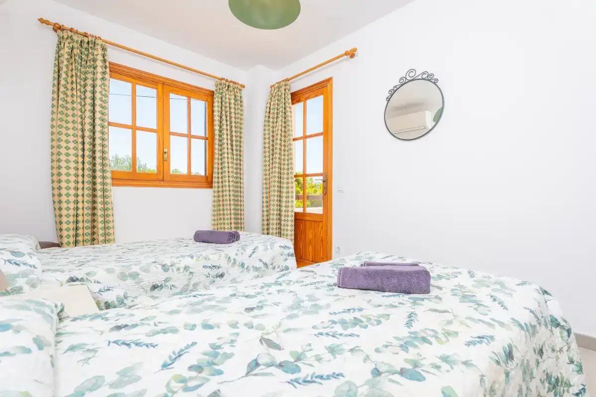 A bright bedroom with floral bedding, curtained windows, and a glass door.