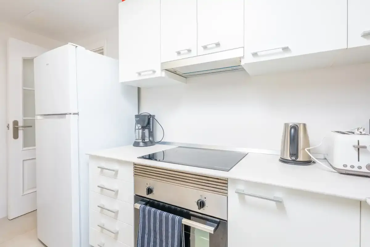 A bright white kitchen with a refrigerator, cooktop, and countertop appliances.