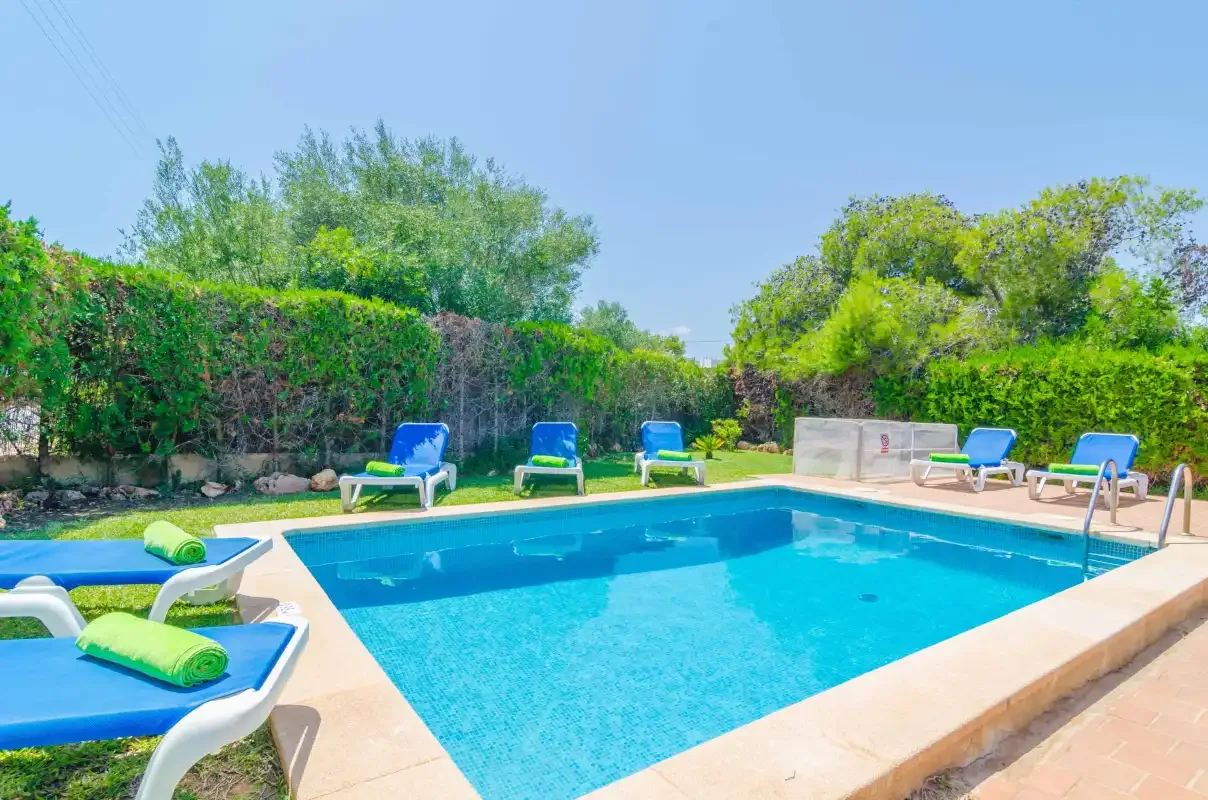 An outdoor swimming pool is surrounded by greenery and lounge seating.
