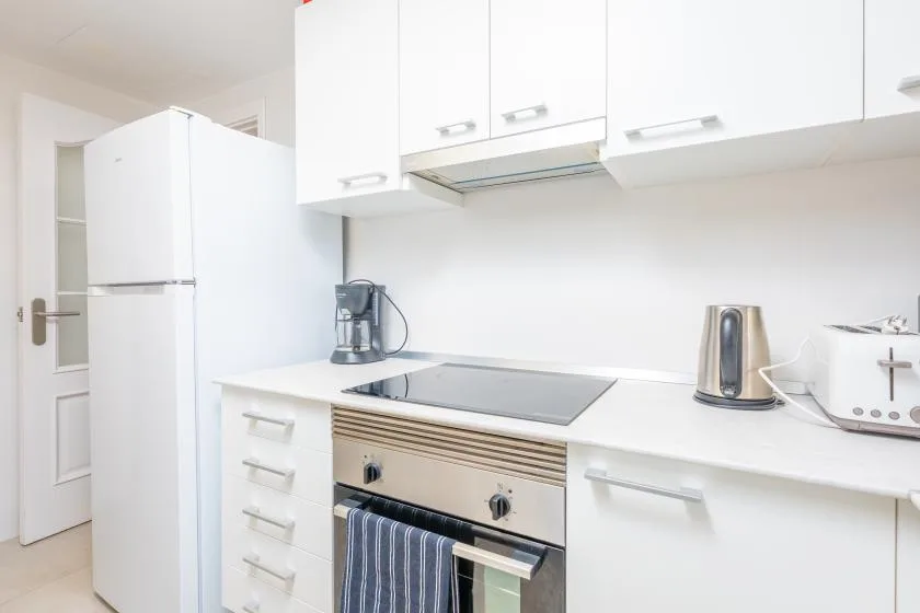 A bright white kitchen with a stovetop, oven, and countertop appliances.