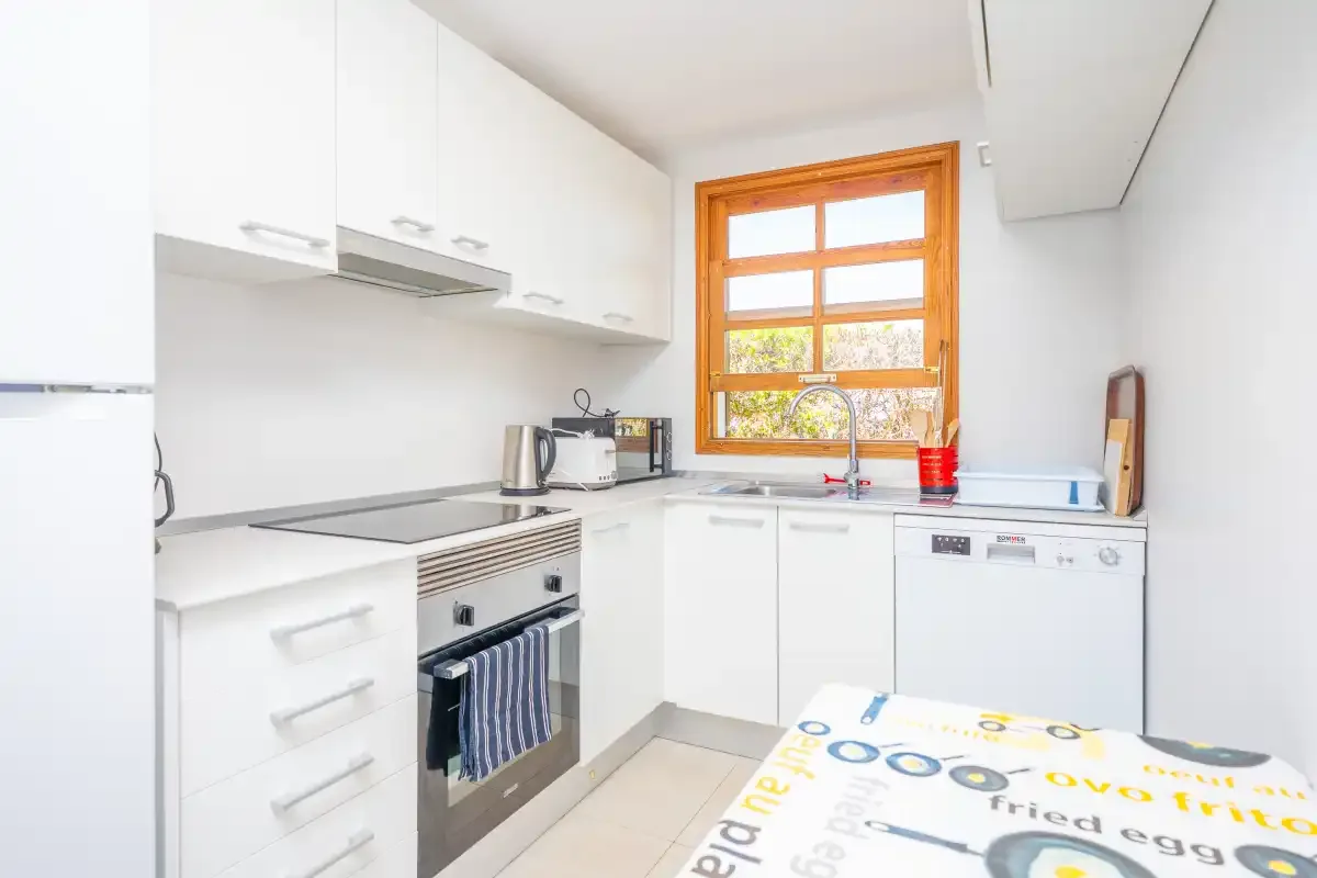 A bright kitchen with white cabinets, a stove, and a window above the sink.