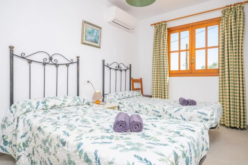 A bedroom with two beds covered in floral bedding beside a bright window.