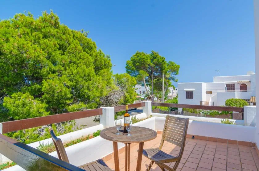 A sunny outdoor terrace has seating, a round table, and leafy trees.