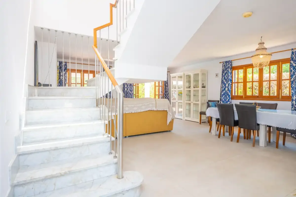 A bright open-plan room with a dining area beside a staircase.