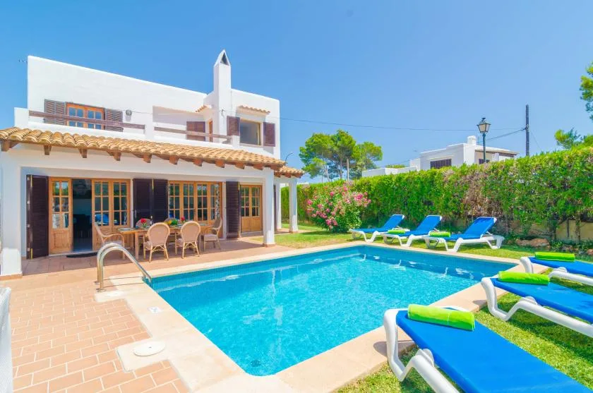 A swimming pool beside a patio and white house, with lounge seating.