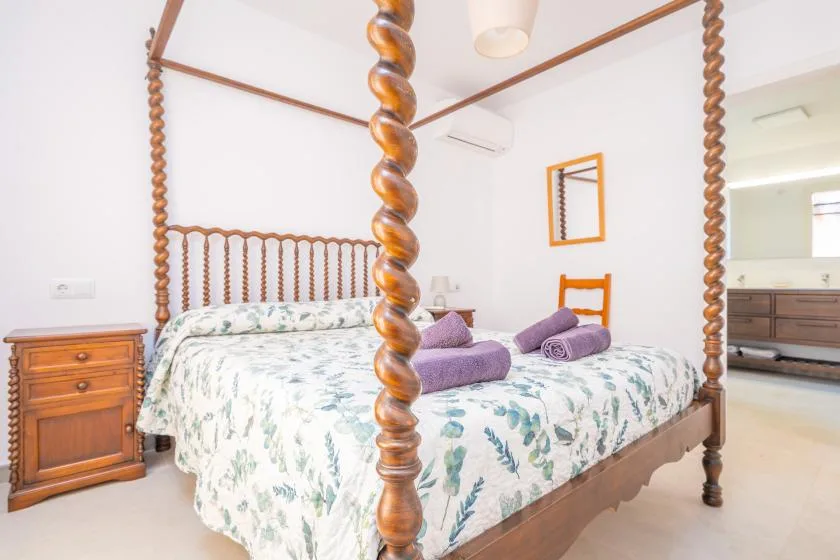 A bedroom with a carved wooden bed, floral bedding, and purple towels.
