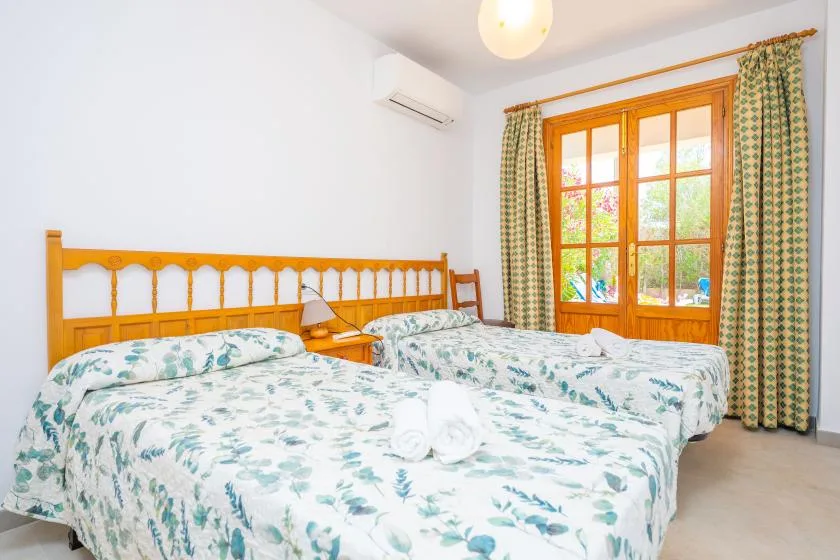 A bright bedroom with two beds and a large wooden-framed window.