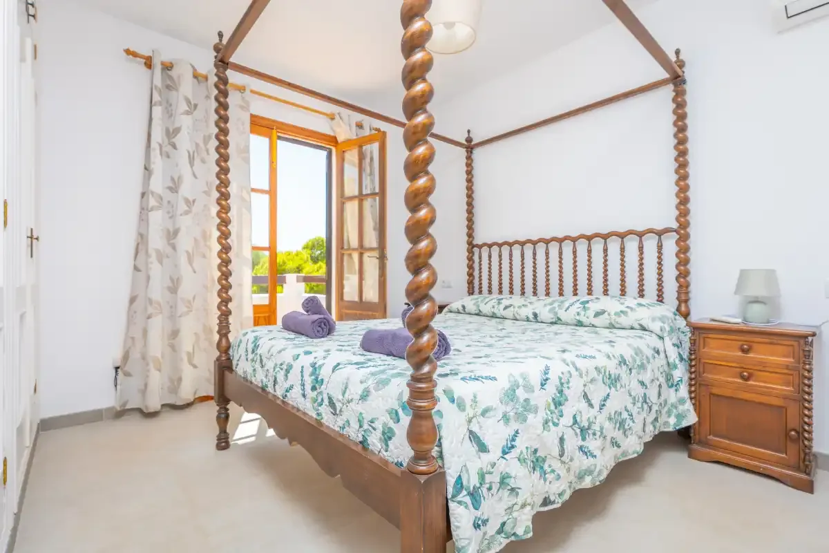 A bedroom with a wooden four-poster bed and an open window.