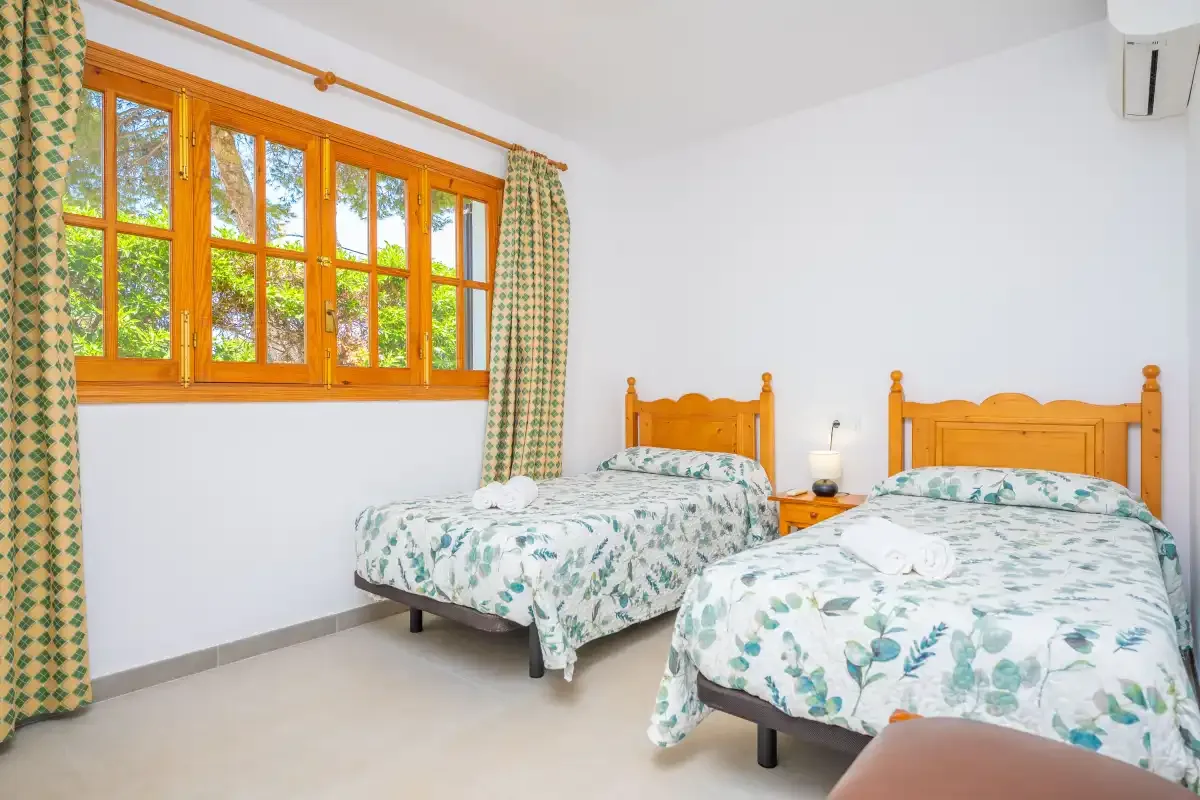 A bright bedroom with two beds beside a large window.