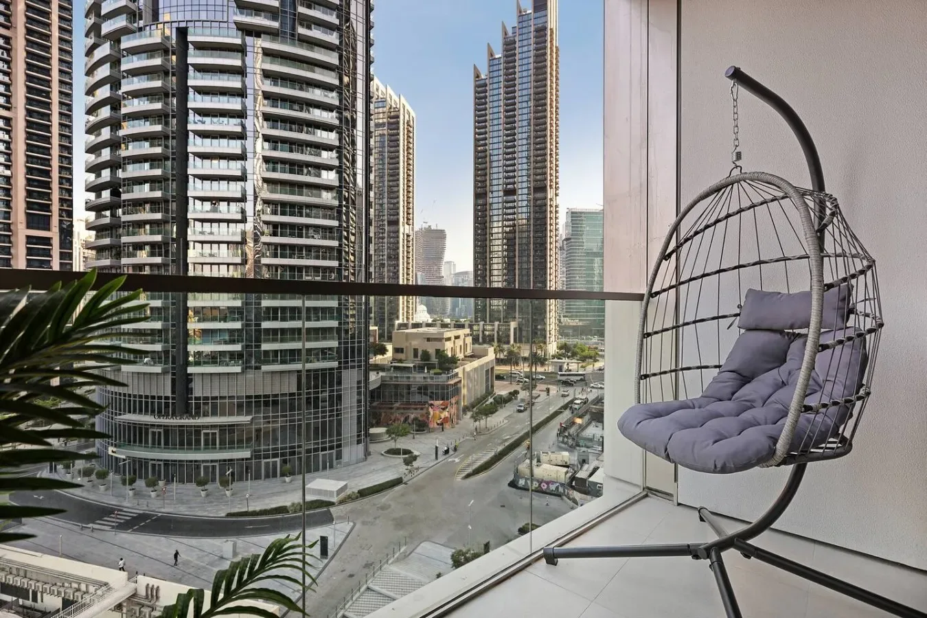 Un balcón da a modernos edificios altos, con un asiento colgante junto a la barandilla de vidrio.