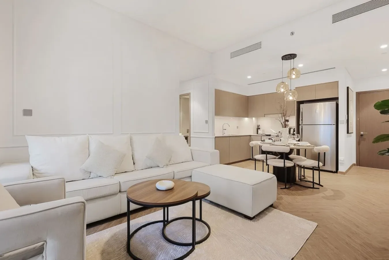 Una sala luminosa con asientos claros y una cocina abierta al fondo.