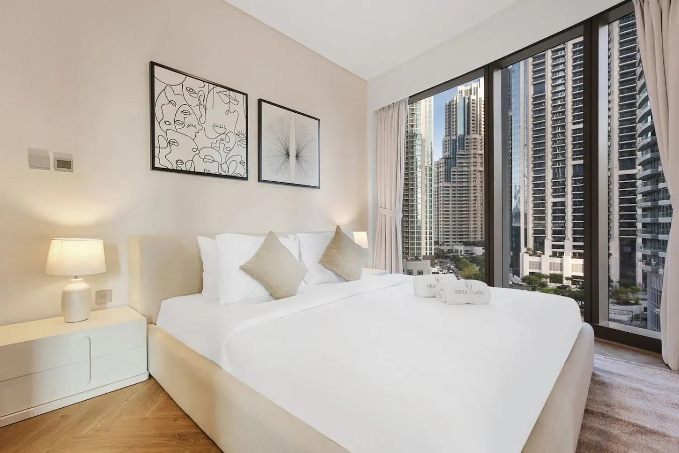 Un dormitorio con una cama tendida junto a ventanales que dan a edificios de la ciudad.