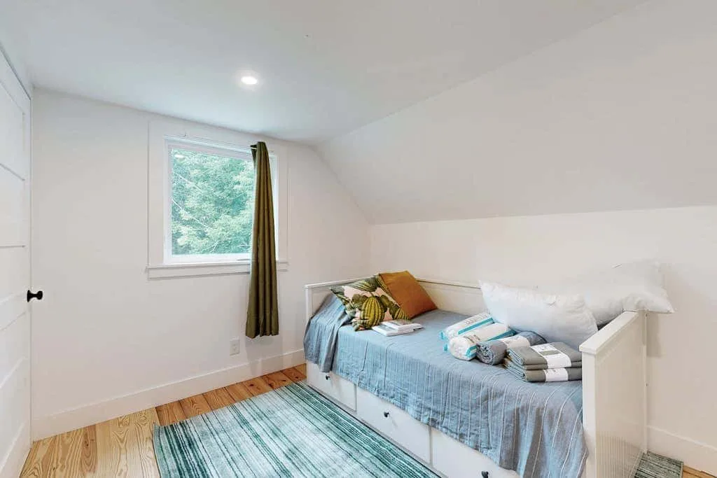 A bright bedroom with a daybed beside a window and a striped rug.