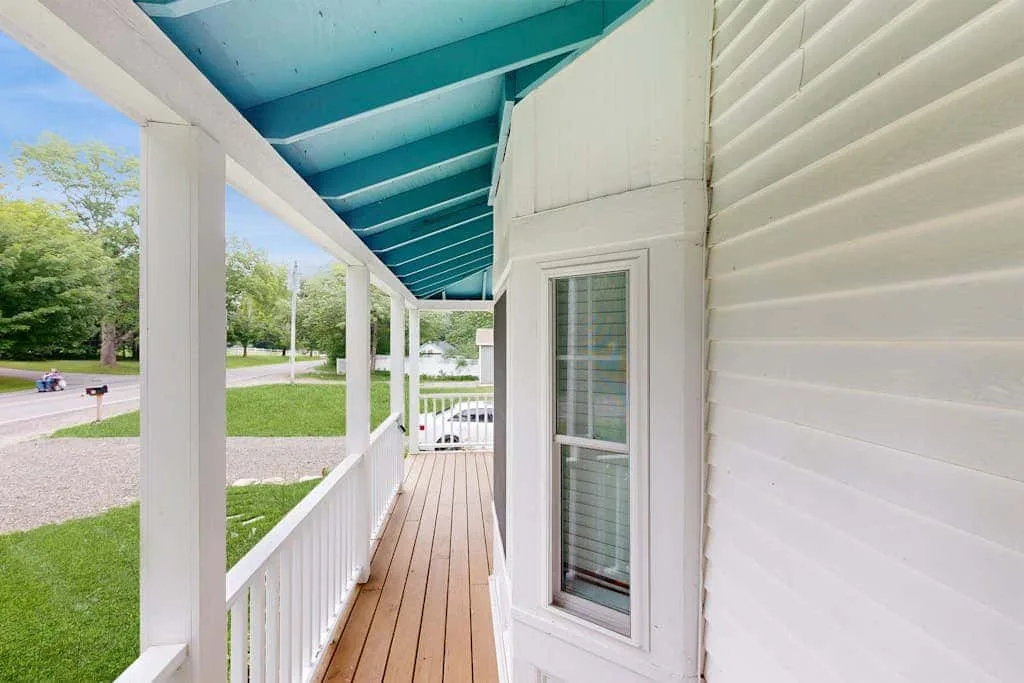 A covered porch with white railings overlooks a grassy roadside area.