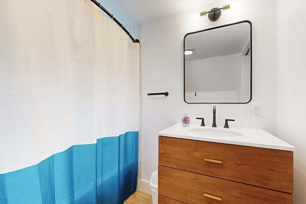 A bathroom with a sink vanity, mirror, and blue-and-white shower curtain.
